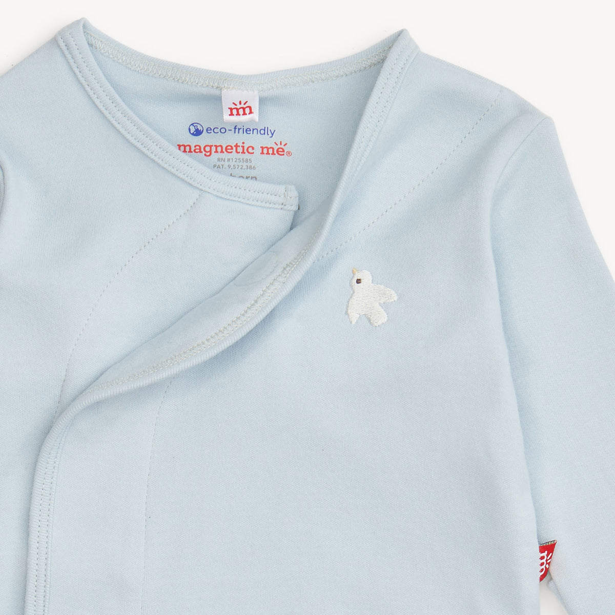 A close-up of a baby long-sleeve wrap top in light blue, featuring a small white embroidered bird on the chest and a visible 'magnetic me' brand label inside the collar.