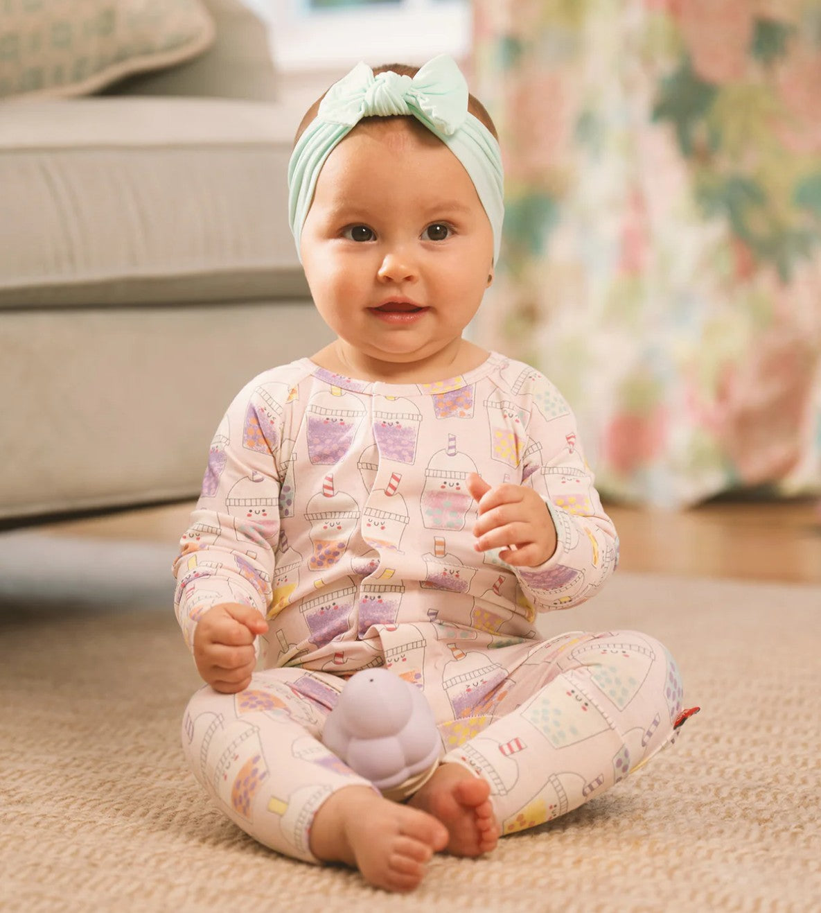 Baby in pastel pajamas with a headband sitting on a carpeted floor.