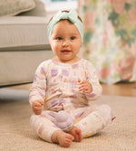 Baby in pastel pajamas with a headband sitting on a carpeted floor.