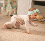 Baby in a patterned onesie and headband crawling on a carpeted floor.