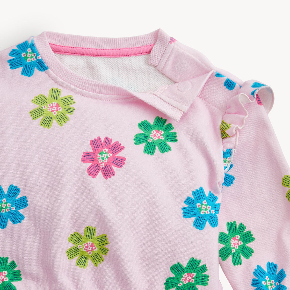 A close-up of a light pink long-sleeve top with colorful embroidered flowers in blue, green, and pink, featuring a ribbed collar and sleeve cuffs.