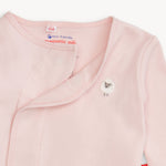 Close-up of a light pink long-sleeve baby wrap or sleeper with a snap closure and a small sheep applique on the chest. The inside neck label shows the brand 'mii' and text reading 'eco-friendly magnetic me.