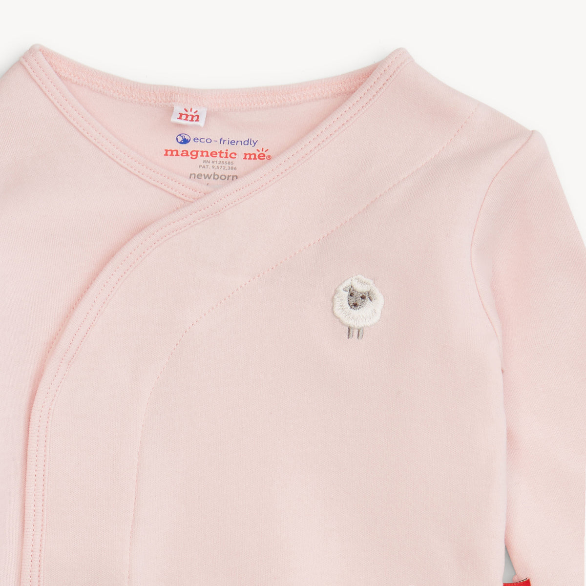 A close-up of a pale pink long-sleeve baby wrap top with a small embroidered sheep face on the chest. The inside neck label shows the Newborn brand and 'eco-friendly magnetic mus' text.