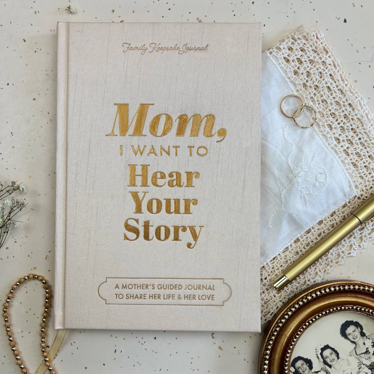 Book titled 'Mom, I Want to Hear Your Story' on a textured surface with lace and rings.