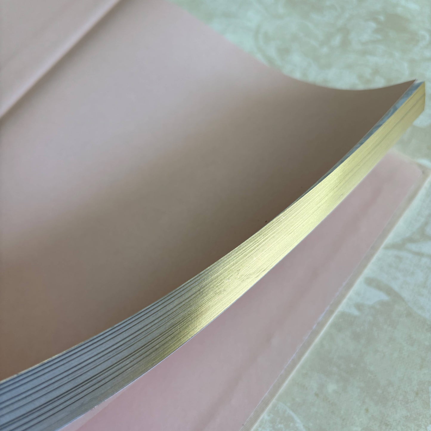 Stack of pink paper with a gold edge on a textured surface