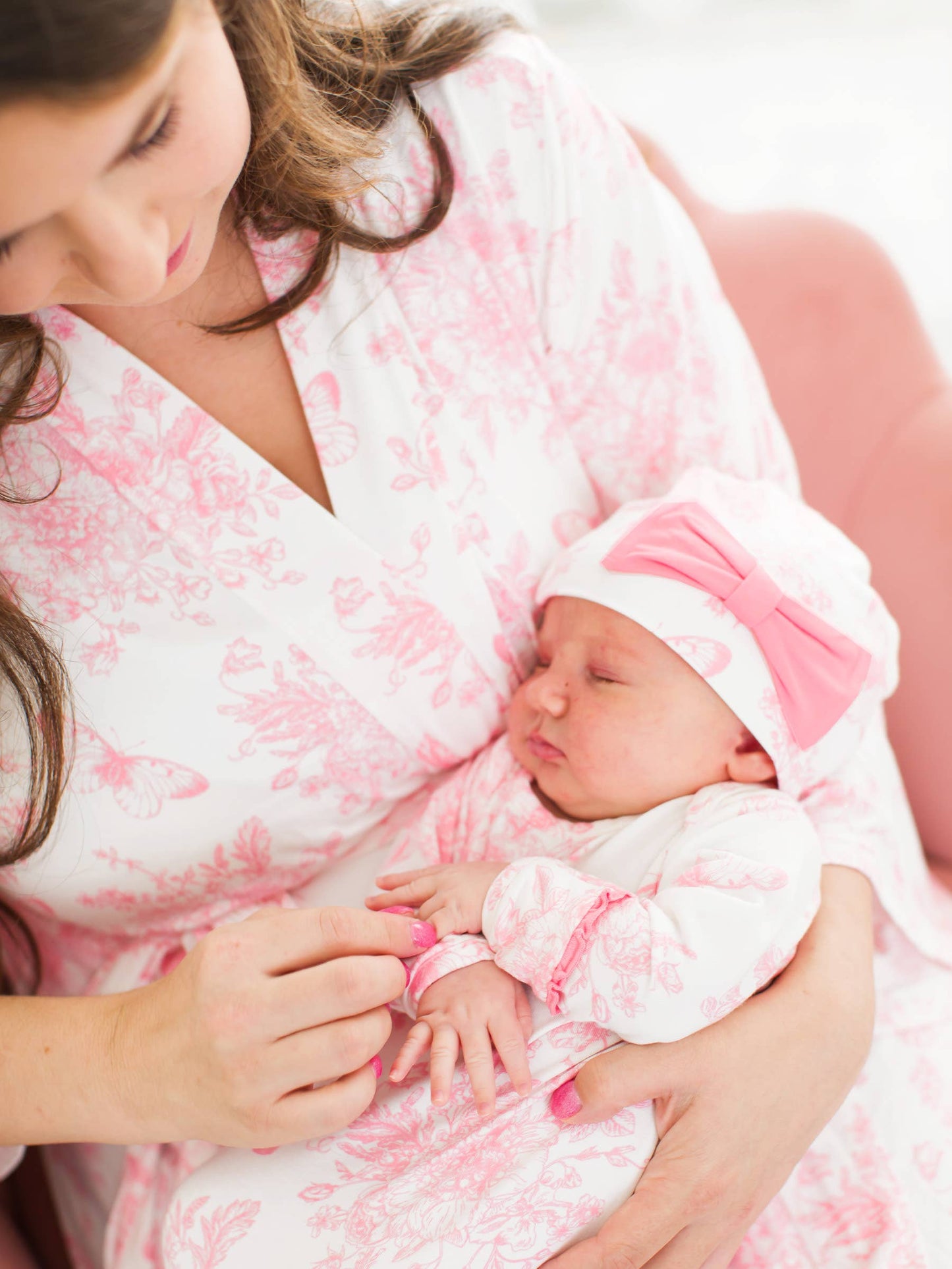 Woman holding a newborn baby wrapped in a pink and white patterned blanket.