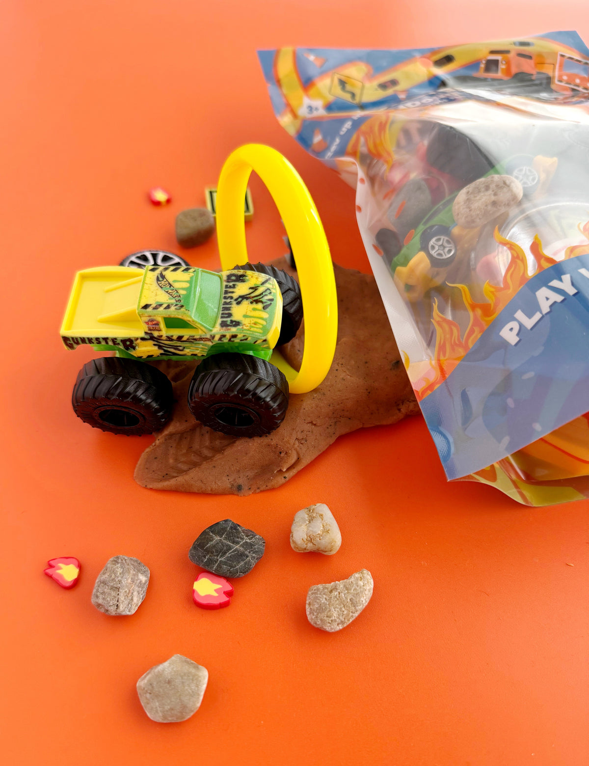 Toy truck with a yellow handle on an orange surface with rocks and a bag of small toys.