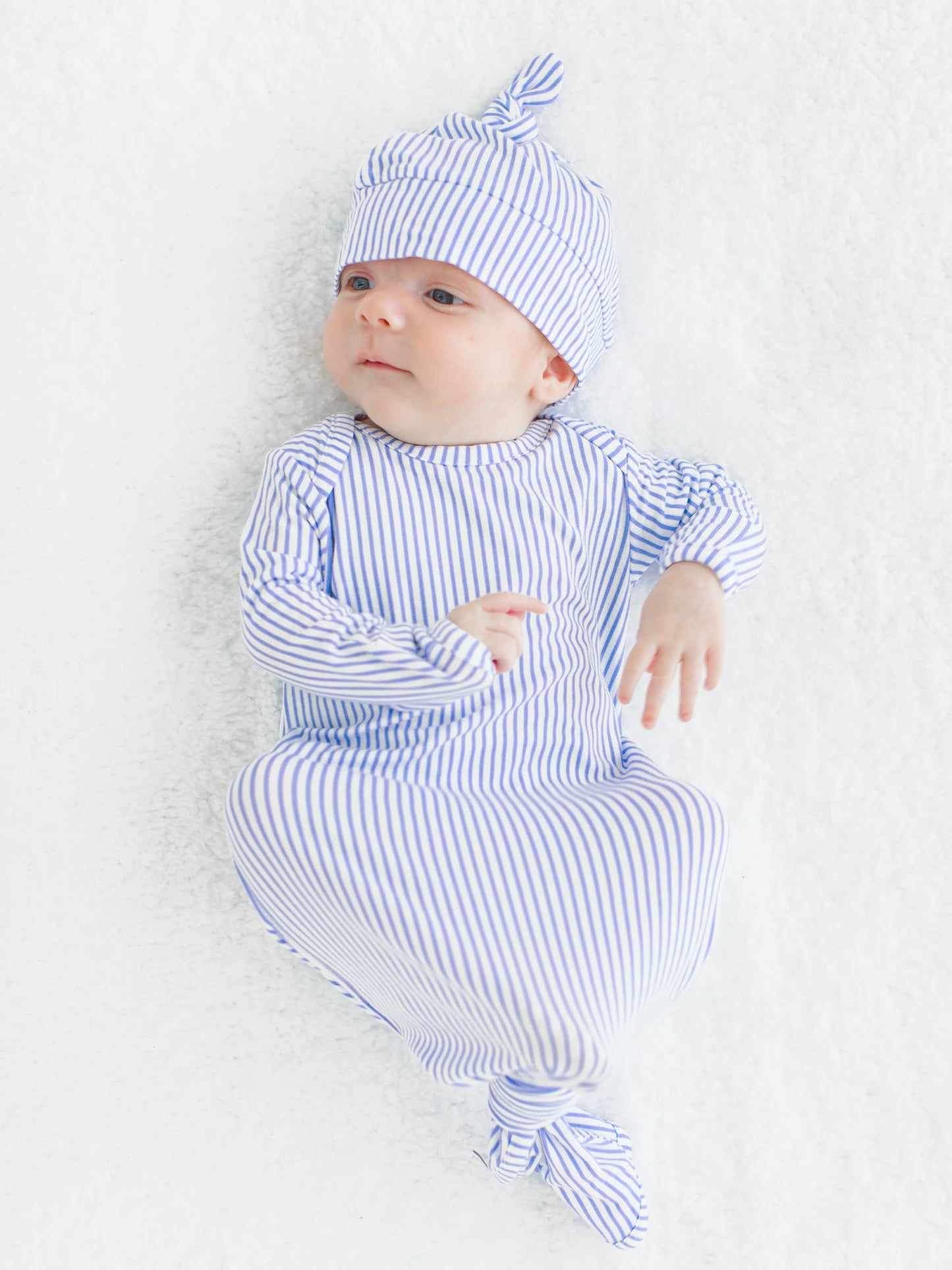 Newborn baby in blue and white striped outfit and hat on a light background