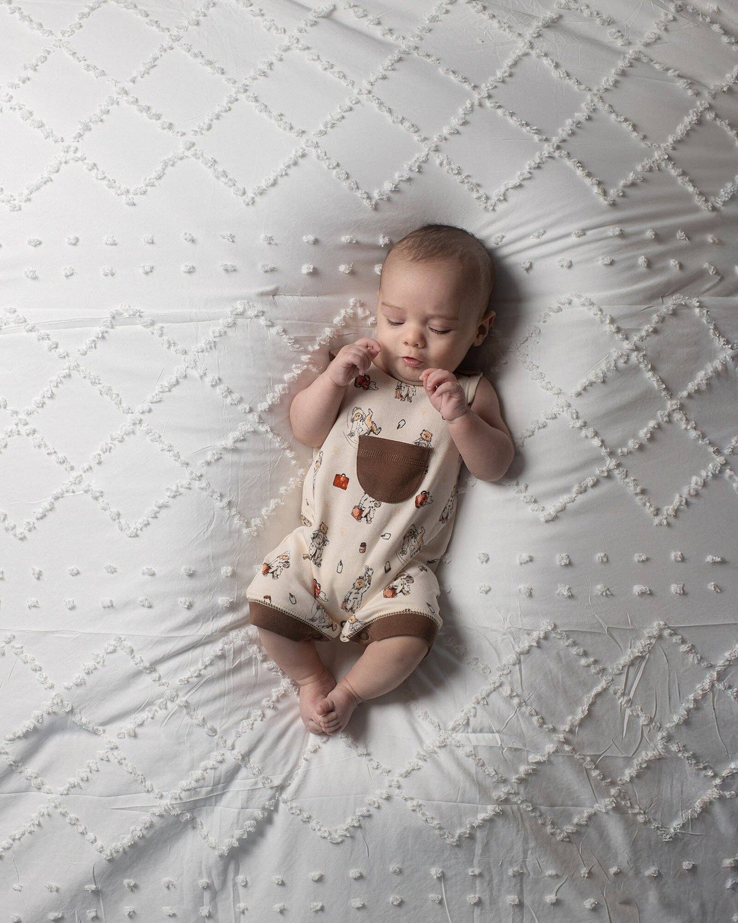 Baby lying on a textured white blanket wearing a Paddington bear overalls