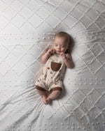 Baby lying on a textured white blanket wearing a Paddington bear overalls