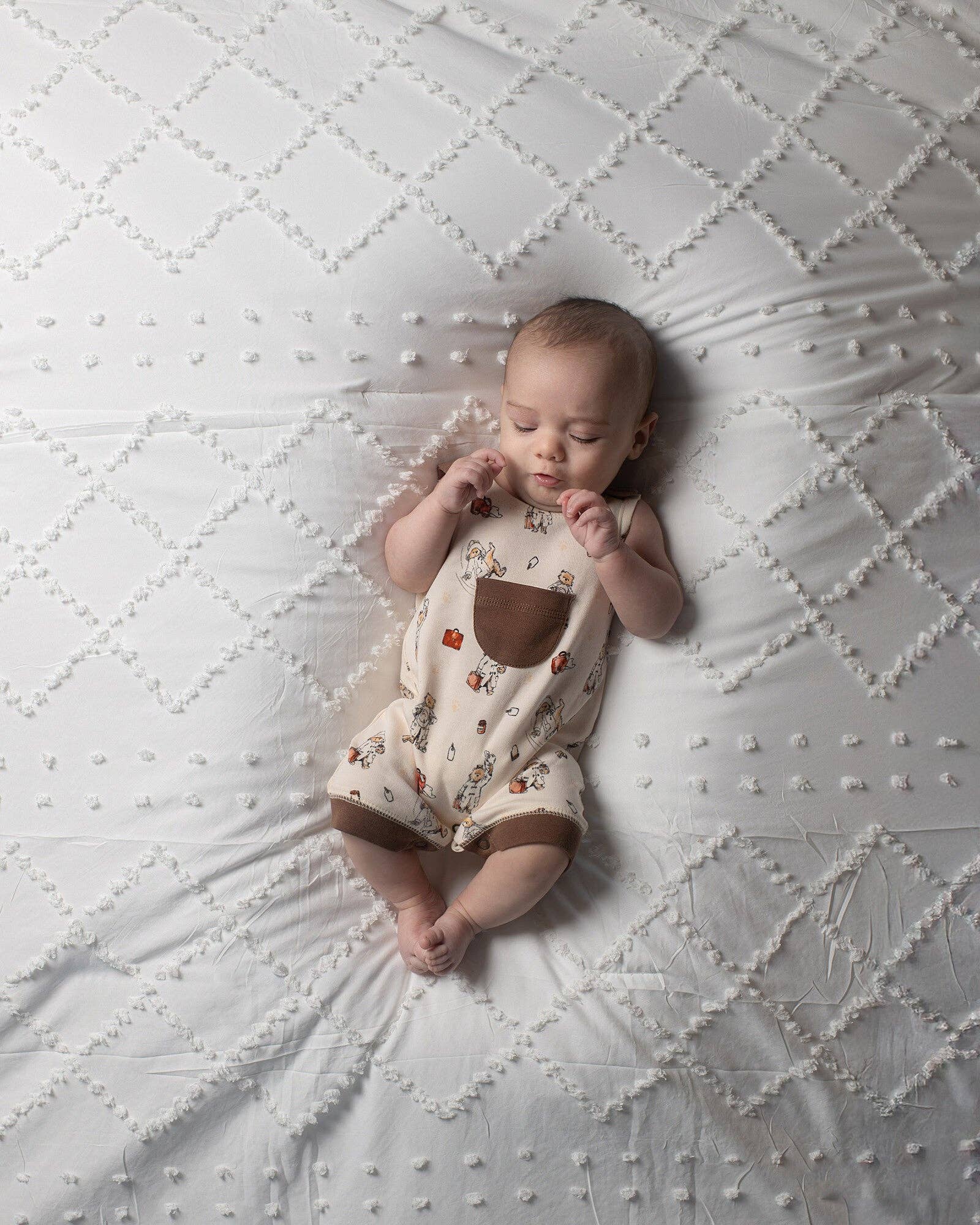 Baby lying on a textured white blanket wearing a Paddington bear overalls
