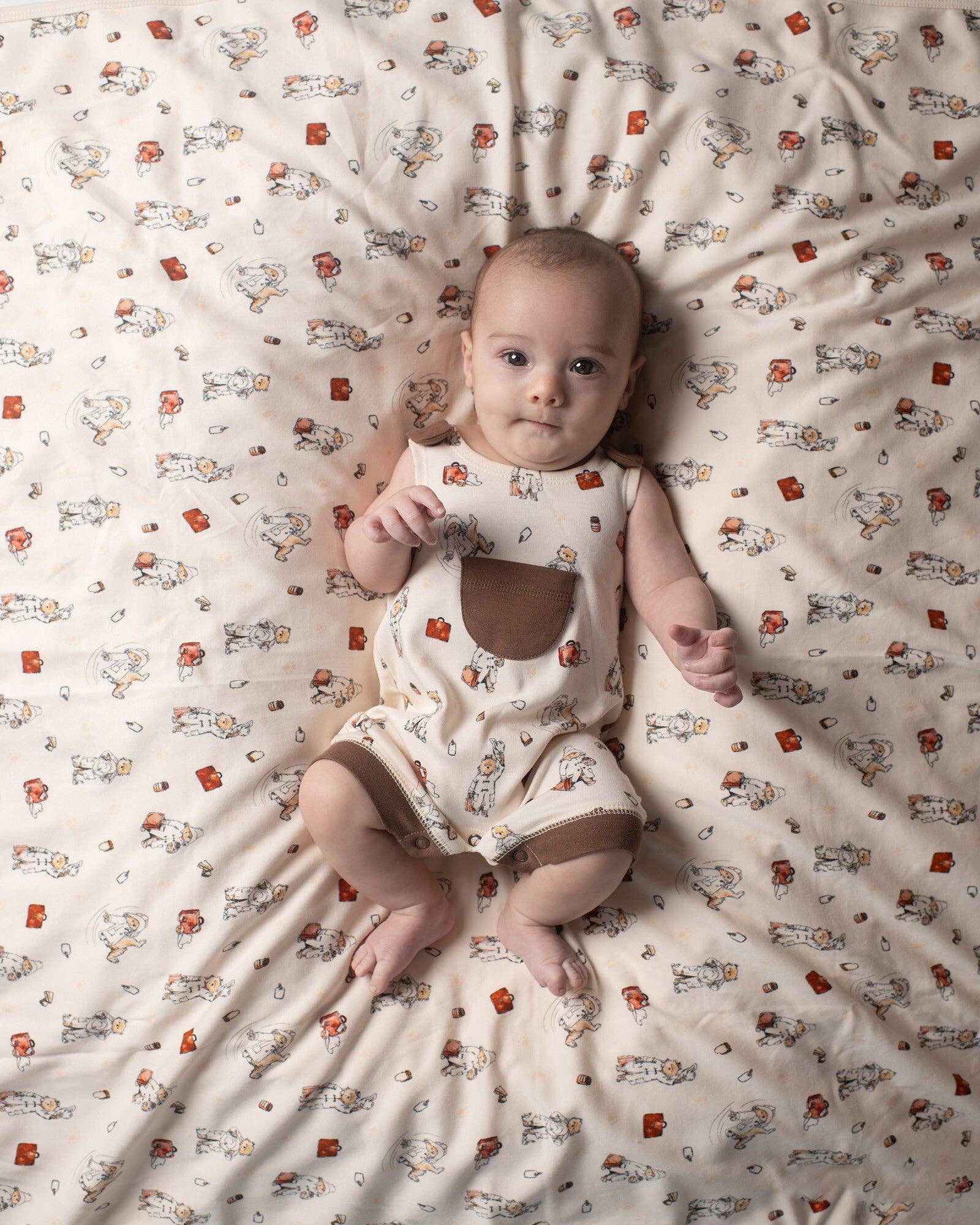 Baby lying on a Paddington bear blanket wearing Paddington bear overalls