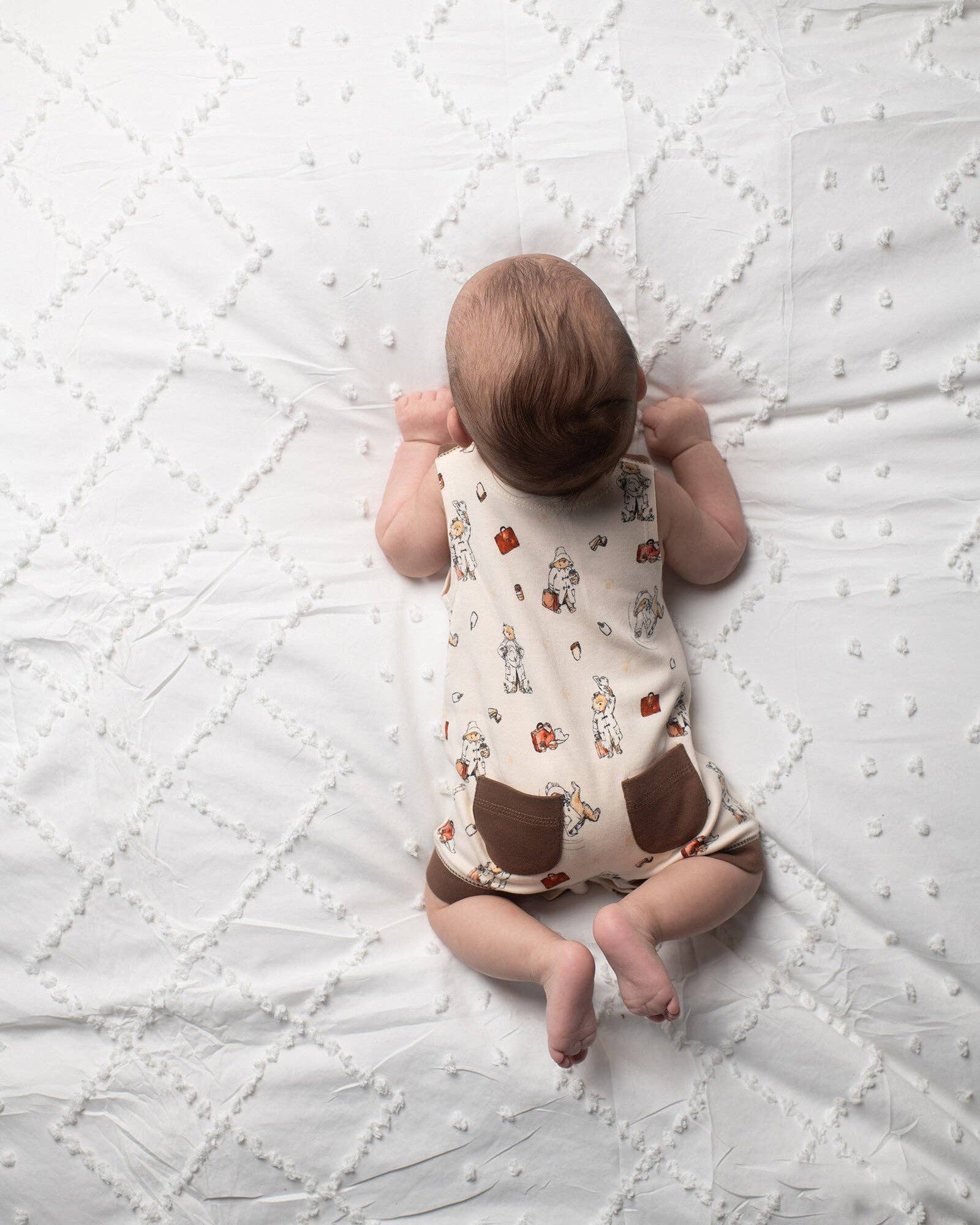 Baby lying on a textured white blanket wearing a patterned outfit.