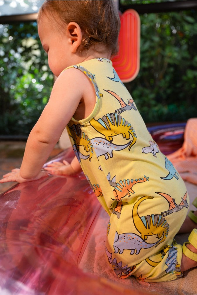 Baby wearing a yellow romper with dinosaur prints on a red inflatable slide.
