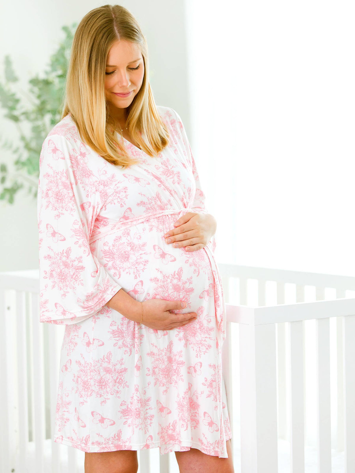 Pregnant woman in a pink floral dress standing in a nursery.
