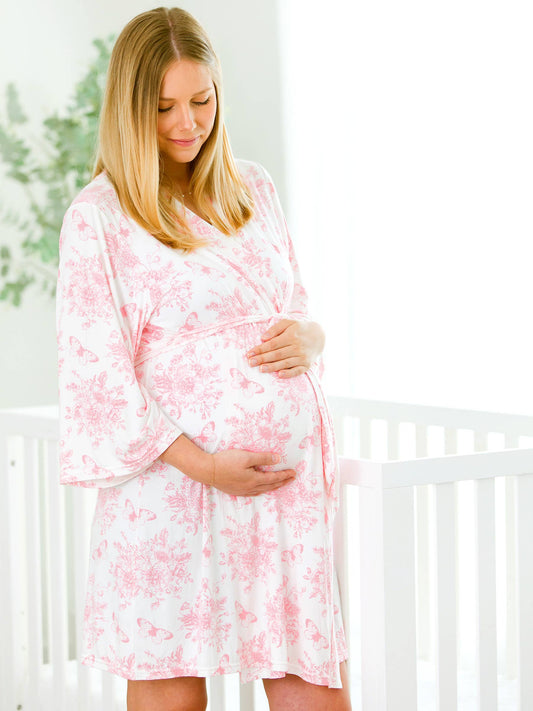 Pregnant woman in a pink floral dress standing in a nursery.