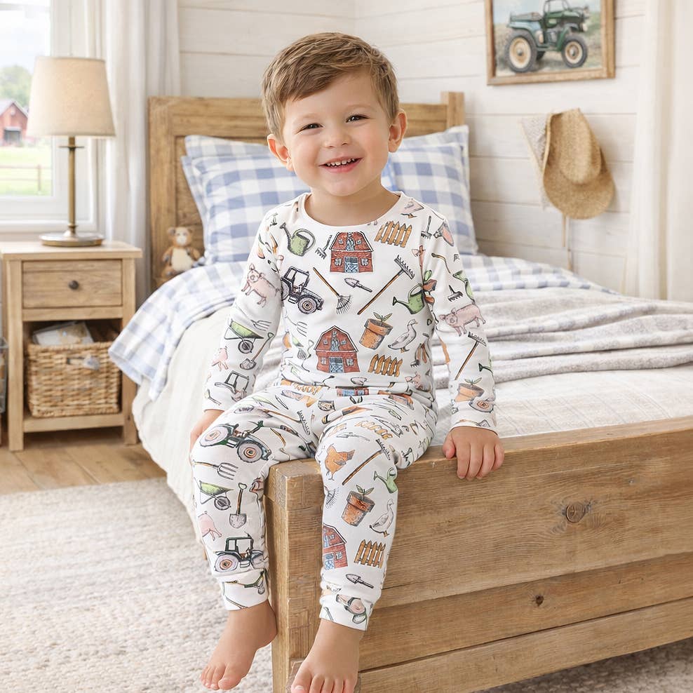 Child wearing pajamas with farm-themed design sitting on a bed in a bedroom.