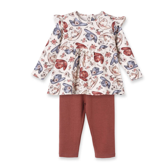 A toddler girl's two-piece outfit featuring a long-sleeve ruffled peplum top with a whimsical cowboy print in red, blue, and brown on an off-white background, paired with rust-colored leggings.