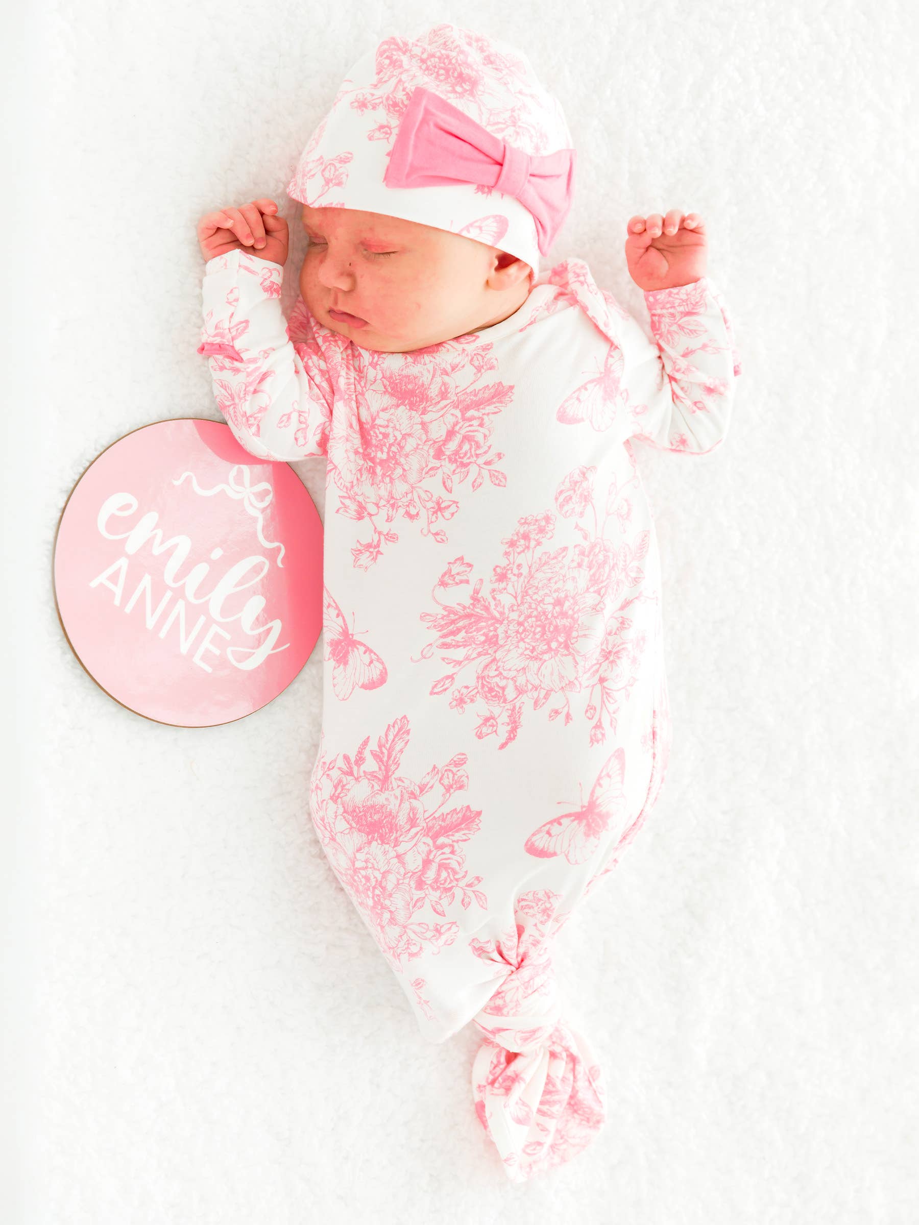 Newborn baby wrapped in a pink floral swaddle with matching hat, lying on a white surface.