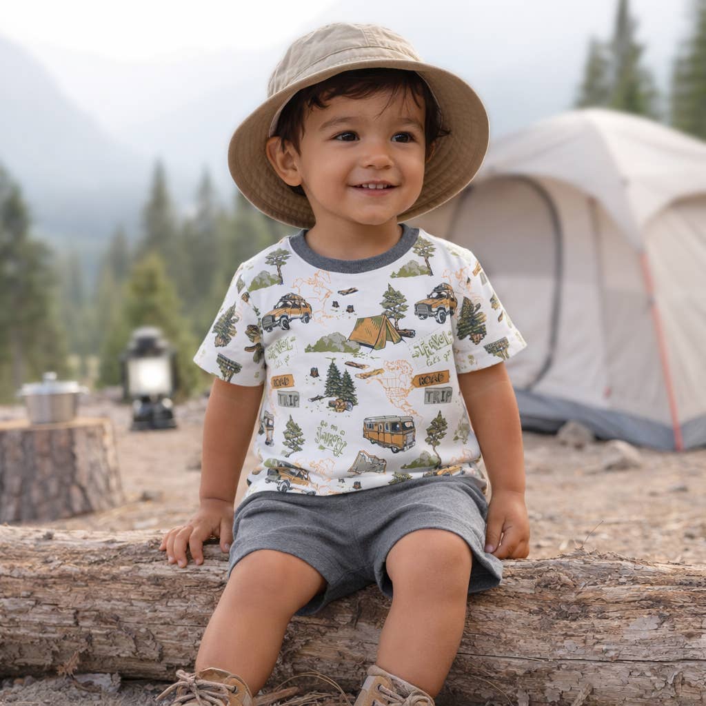 Child sitting on a log in a camping setting with a tent and campfire in the background.