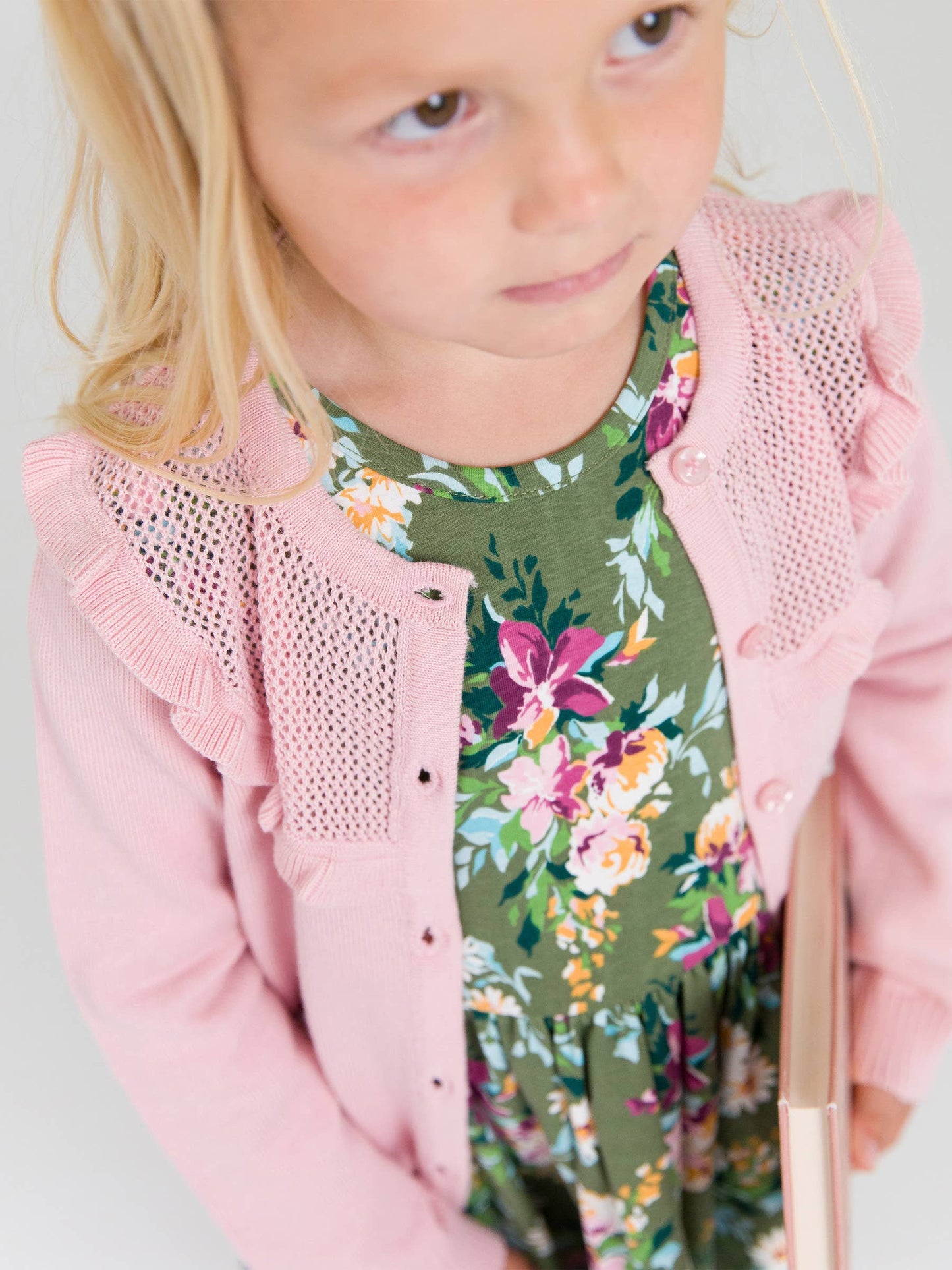 Child wearing a pink cardigan over a floral dress with a neutral background