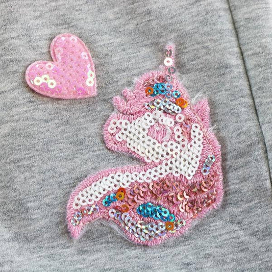 Pink sequin unicorn with heart design on a gray fabric background