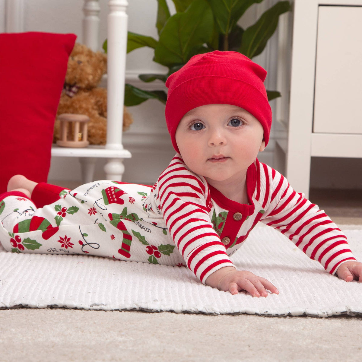 Baby in holiday outfit lying on a rug with a teddy bear in the background