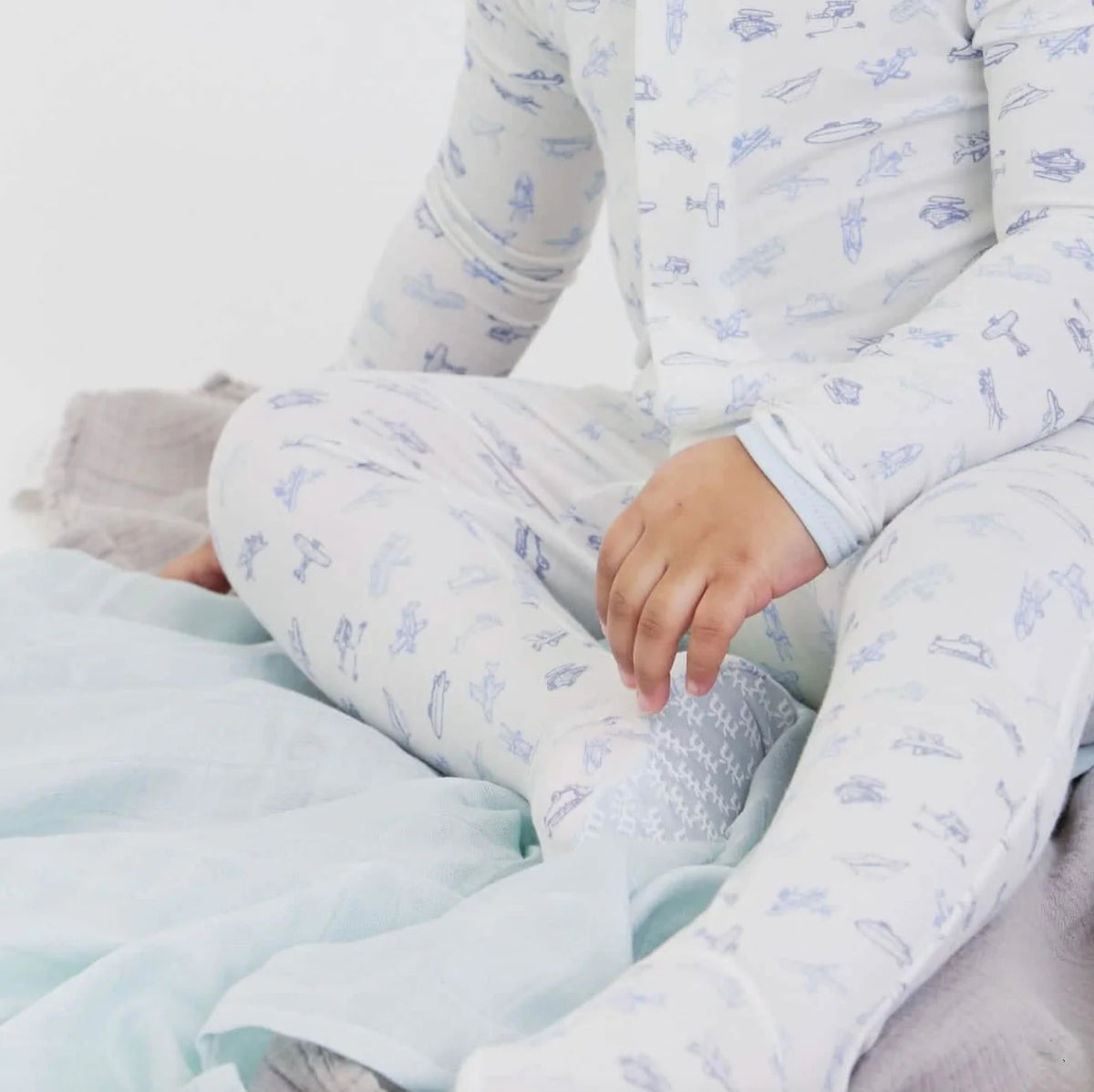 Child wearing a white onesie with blue airplane pattern, sitting on a light blue blanket.