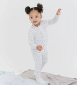Child in a light blue onesie with a airplane pattern, standing on a bed with a white background