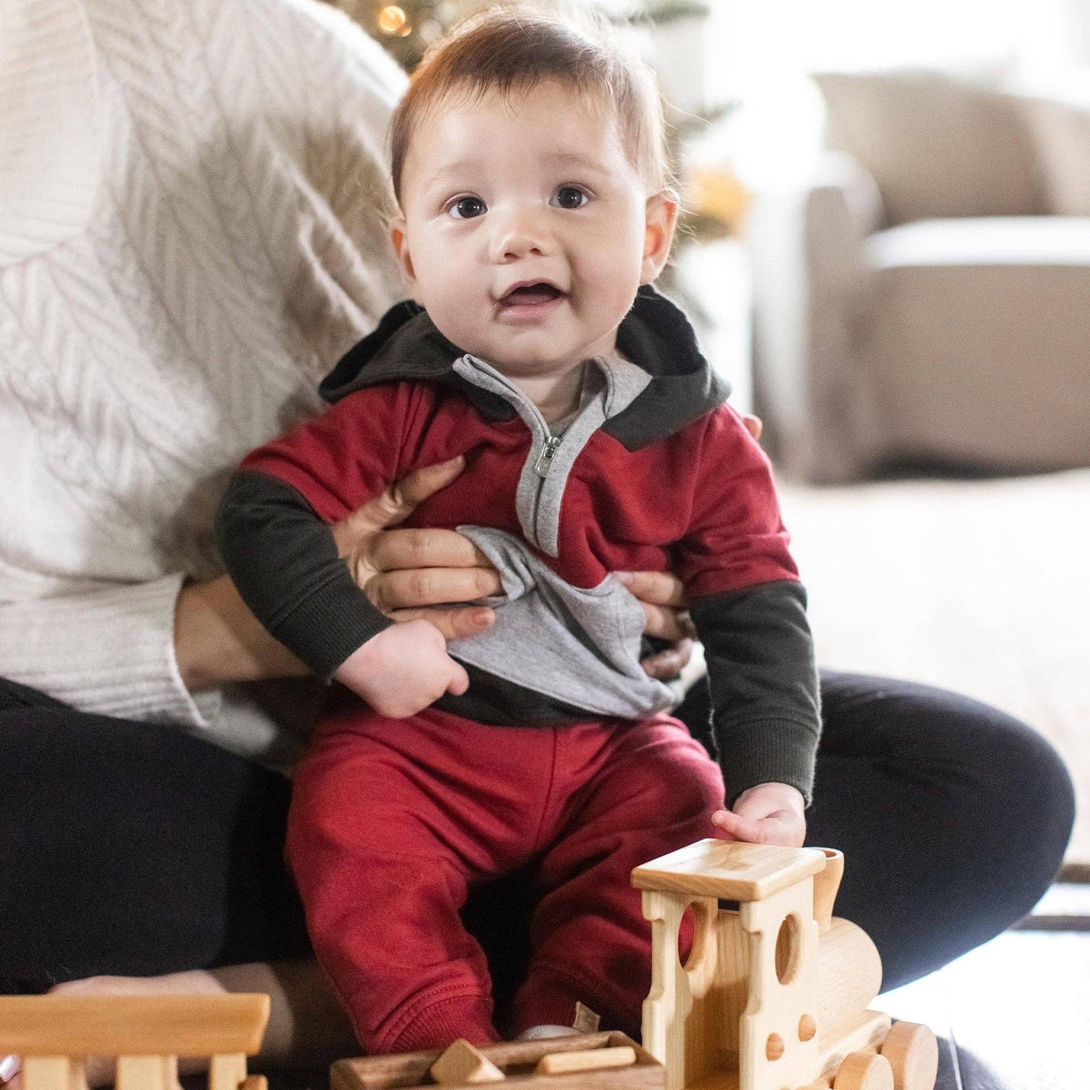 Baby in red and black outfit sitting on a lap with wooden toys