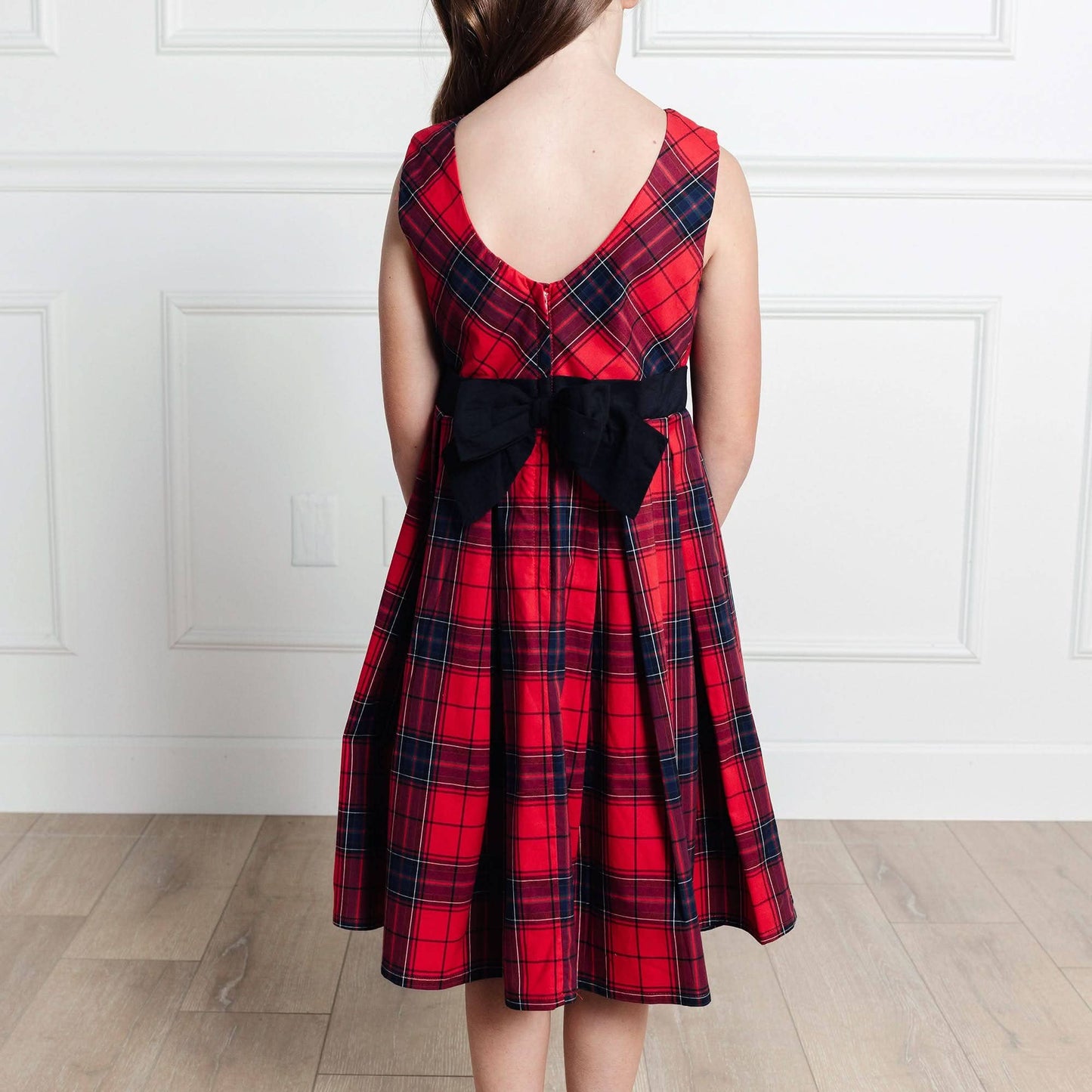 Red plaid dress with a black bow on a white paneled wall background