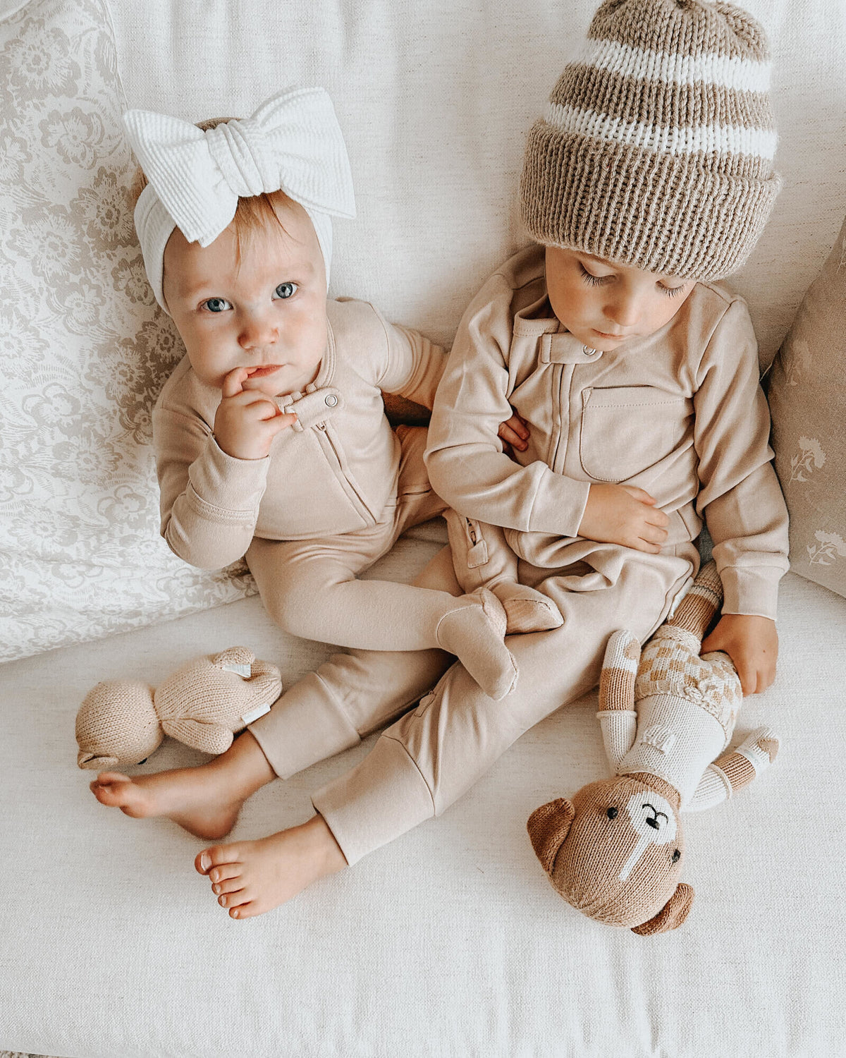 Two children in matching outfits with stuffed animals on a soft surface