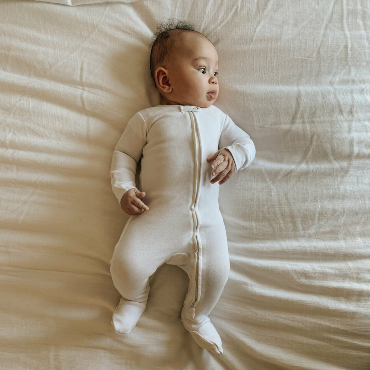 Baby in a cream onesie lying on a beige bed
