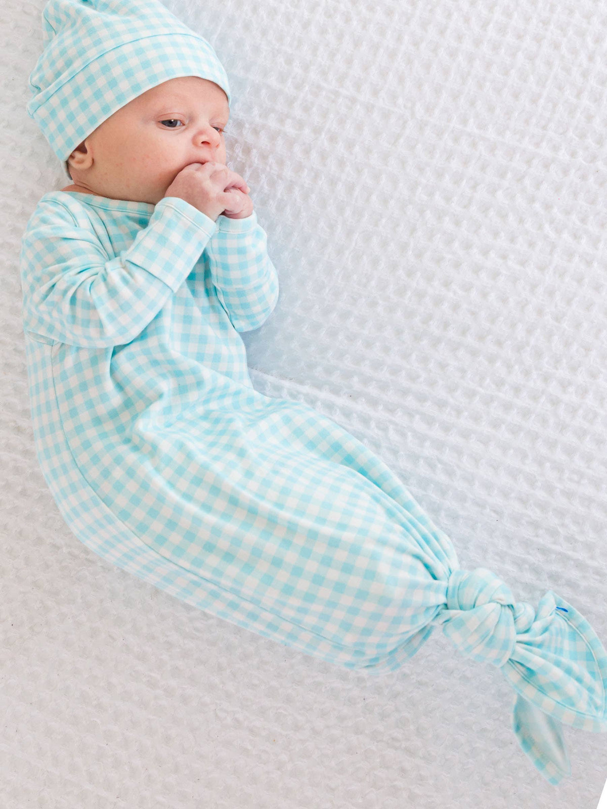 Newborn baby in a light blue checkered outfit lying on a textured white blanket