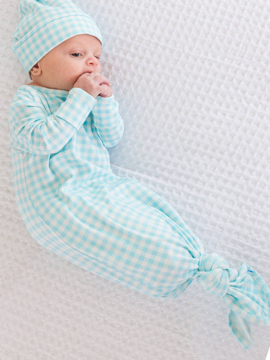 Newborn baby in a light blue checkered outfit lying on a textured white blanket