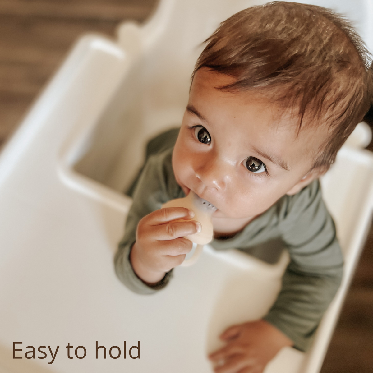 Child in a high chair holding a self feeding pacifier with text 'Easy to hold' below.