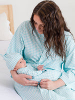 Woman in a light blue checkered robe holding a baby in a matching outfit on a white bed.