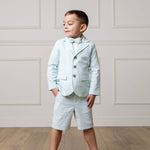 Young boy in a mint suit with a bow tie standing against a white paneled wall.