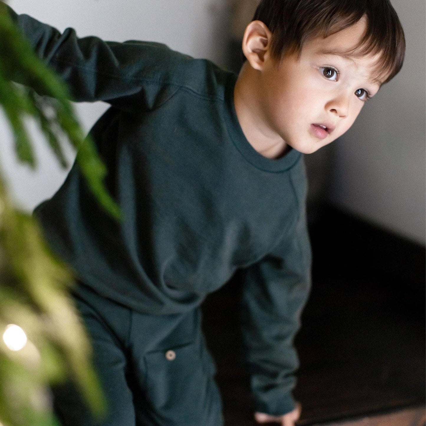 Child wearing a dark green jogger set standing indoors with a neutral background