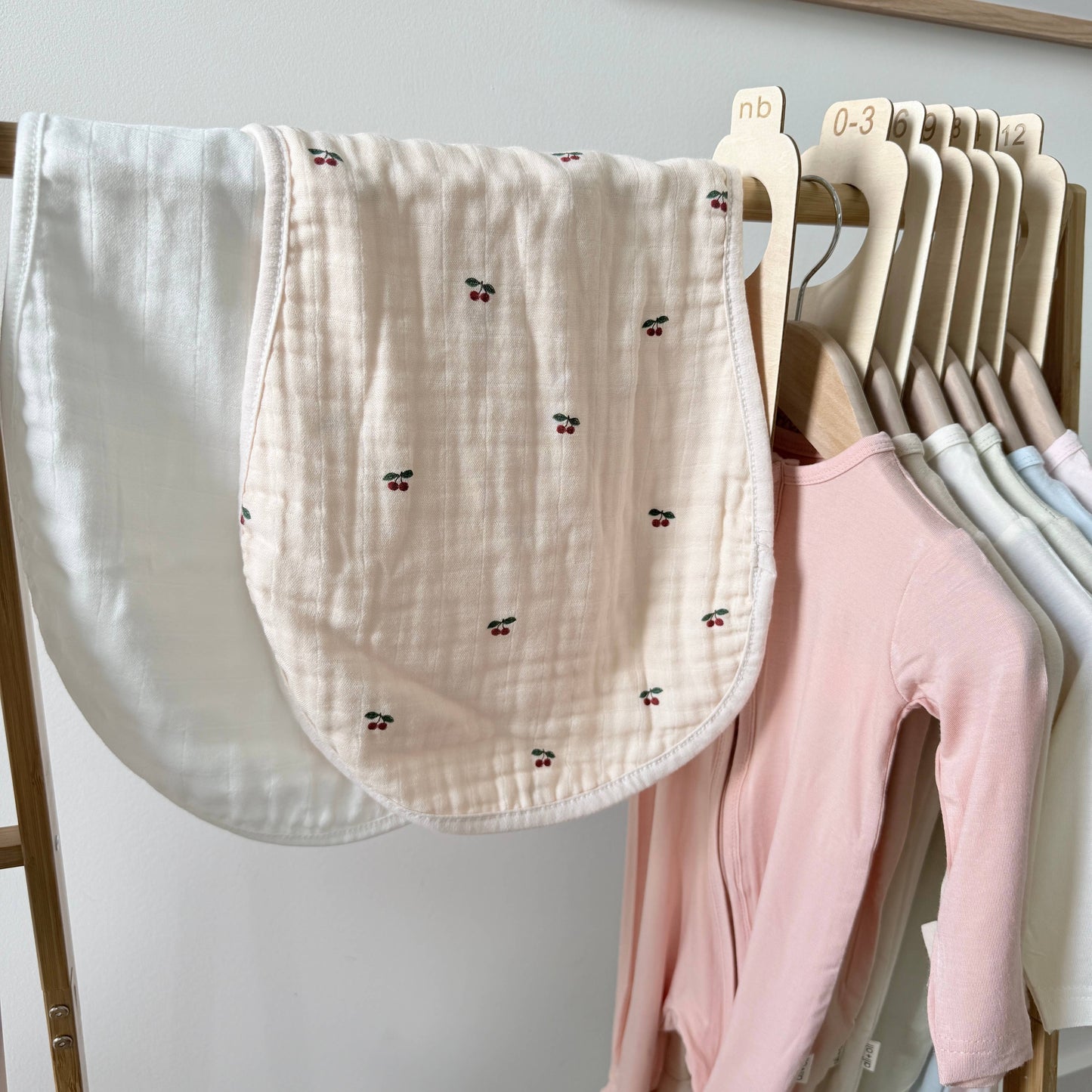 Baby clothes and burp cloths hanging on a rack against a white wall.