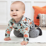 Baby wearing a patterned outfit with pumpkins and cats, crawling on a light-colored surface.