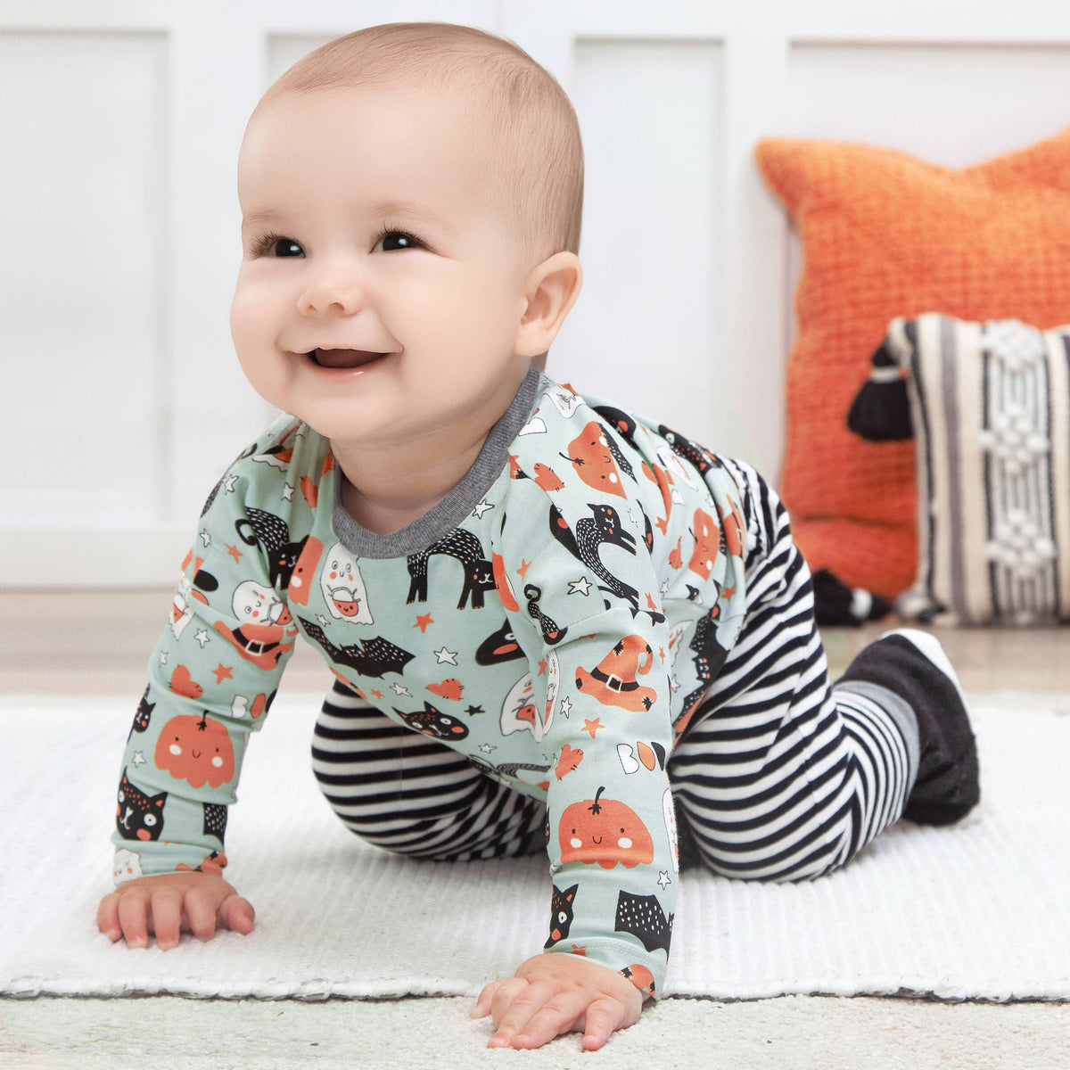 Baby wearing a patterned outfit with pumpkins and cats, crawling on a light-colored surface.