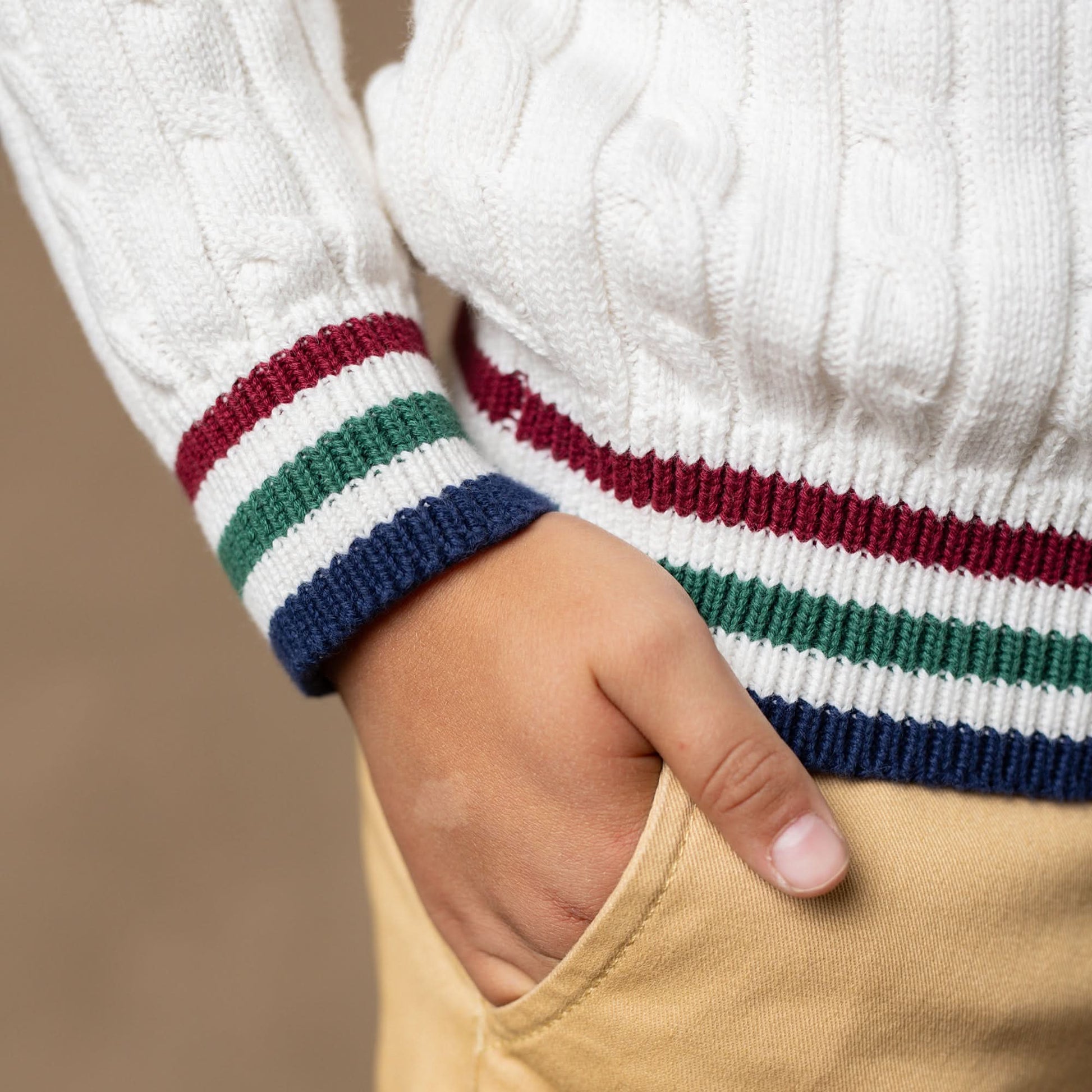 Close-up of a child's hand wearing a white sweater with colorful cuffs.