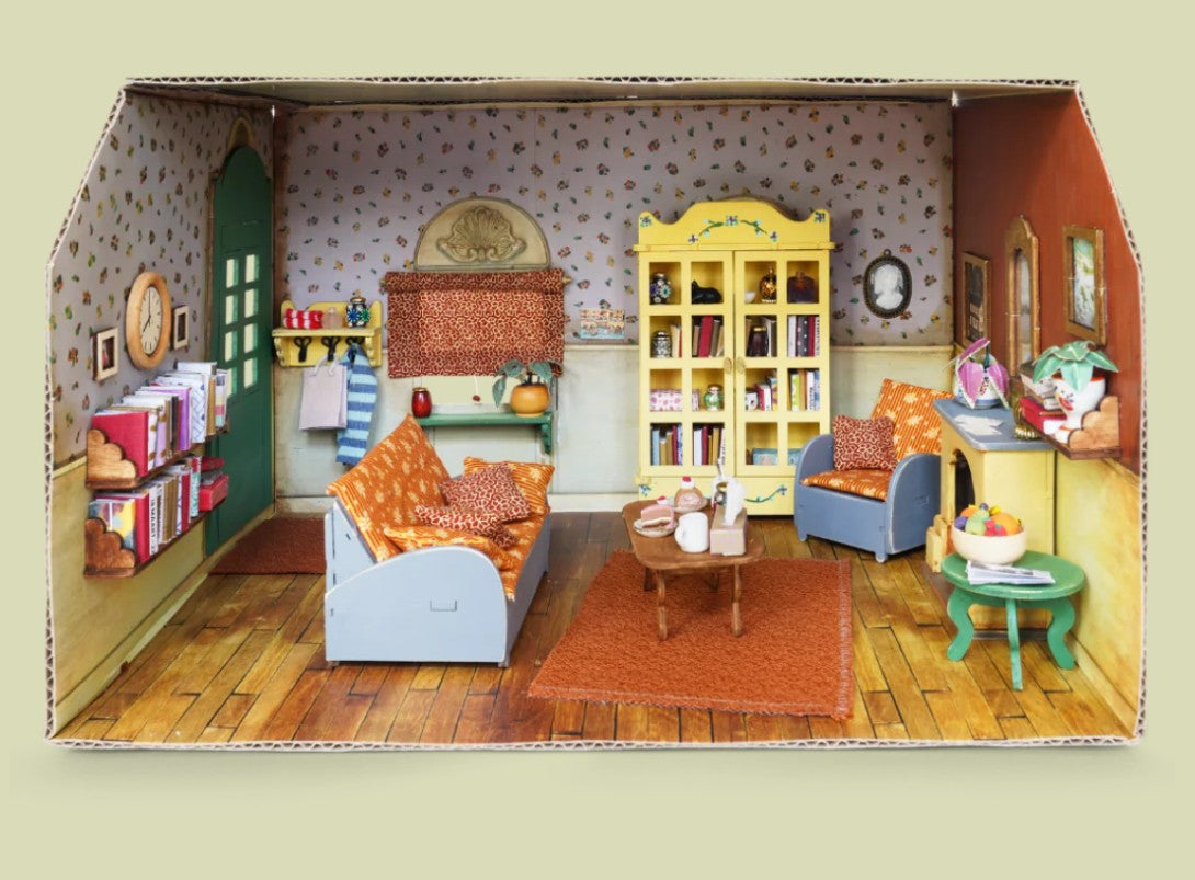 Miniature dollhouse living room set in a cardboard box with furniture and decor.