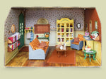 Miniature dollhouse living room set in a cardboard box with furniture and decor.