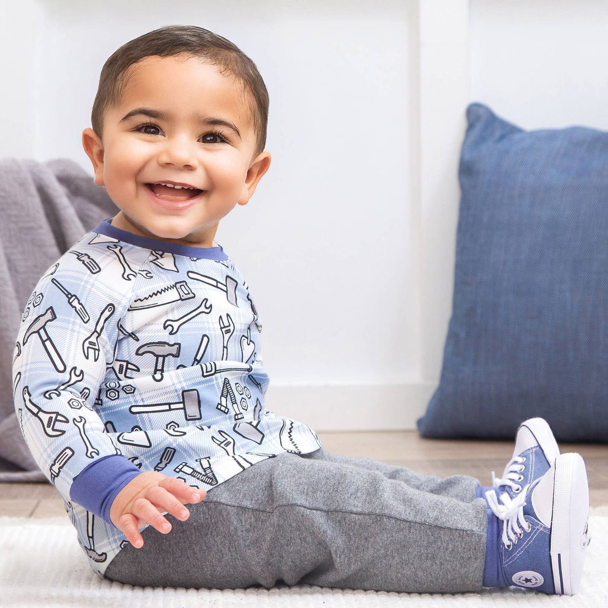 Child wearing 2 piece outfit with tool pattern sitting on a couch