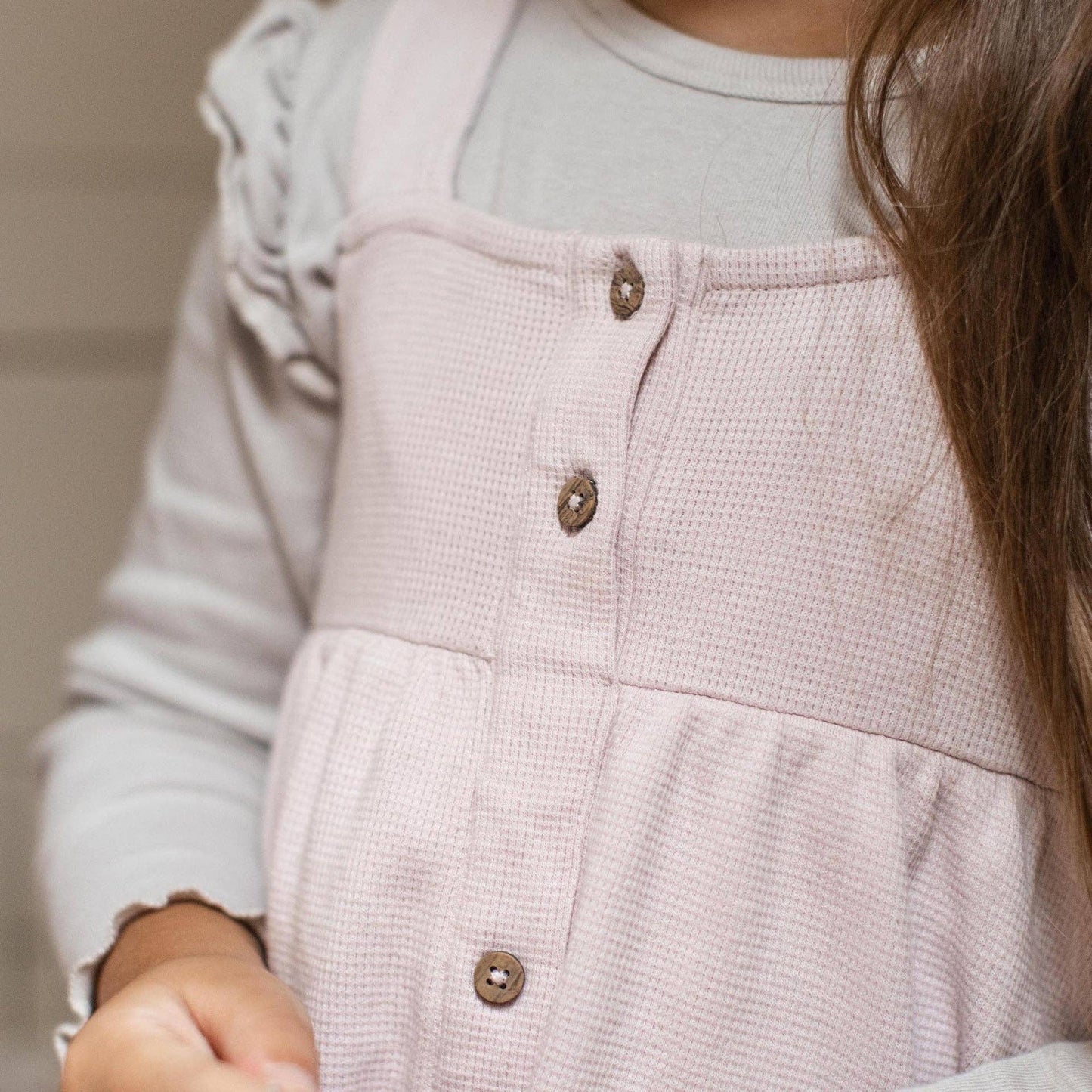Close-up of a light pink dress with buttons on a neutral background