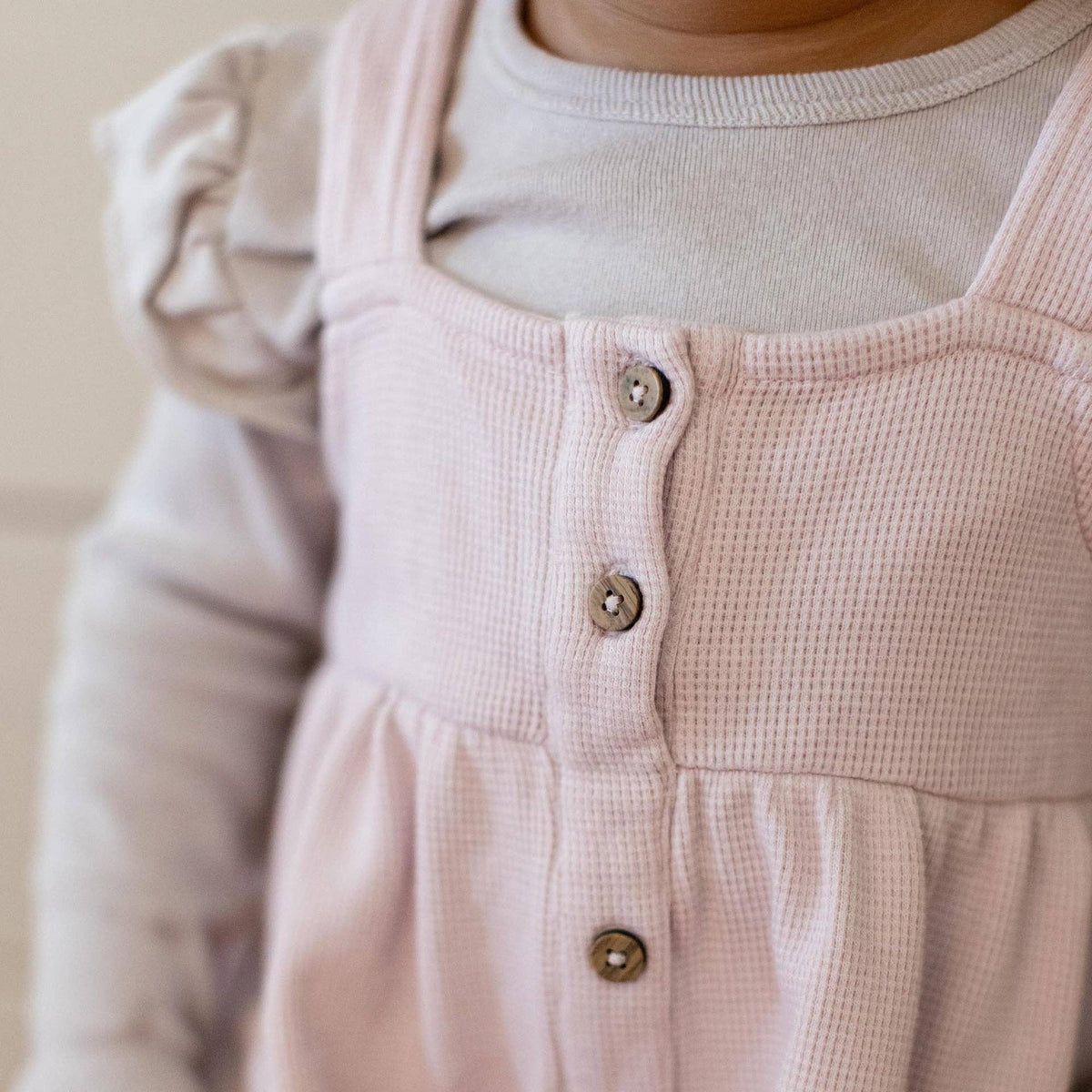Close-up of a pink textured dress with buttons on a neutral background