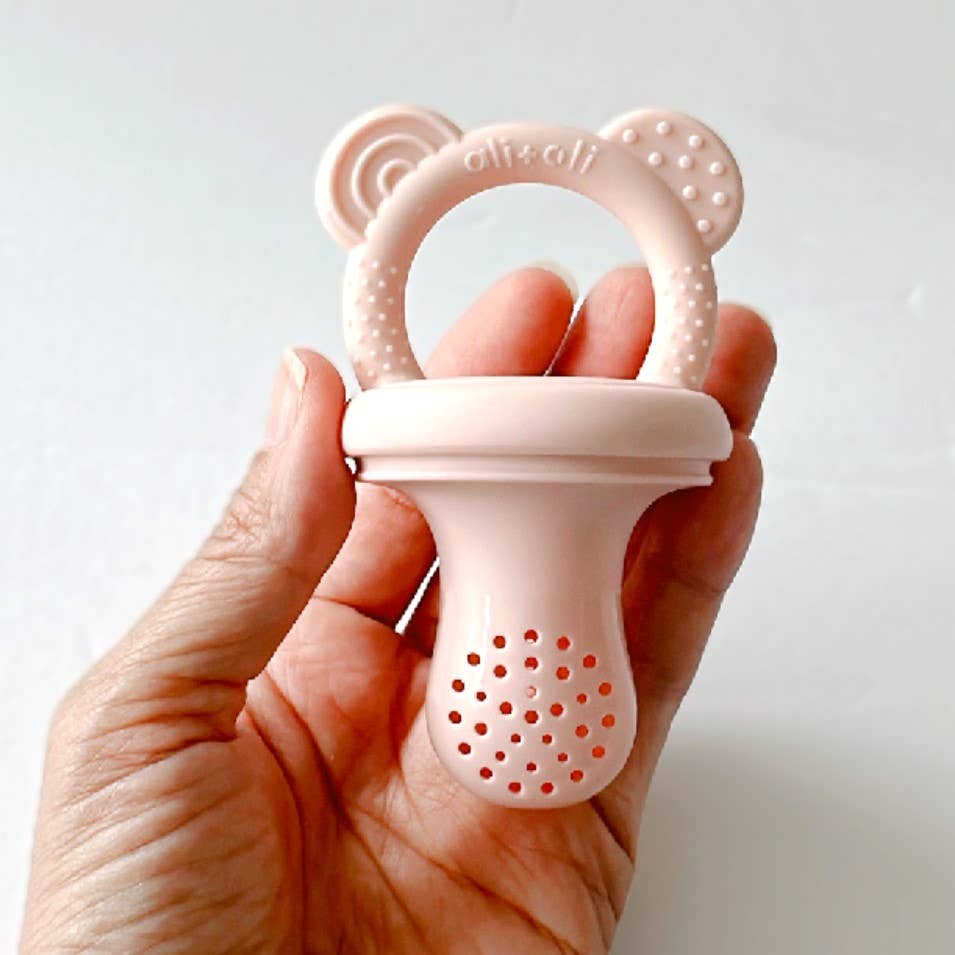 Pink baby self feeding pacifier held in a hand against a white background