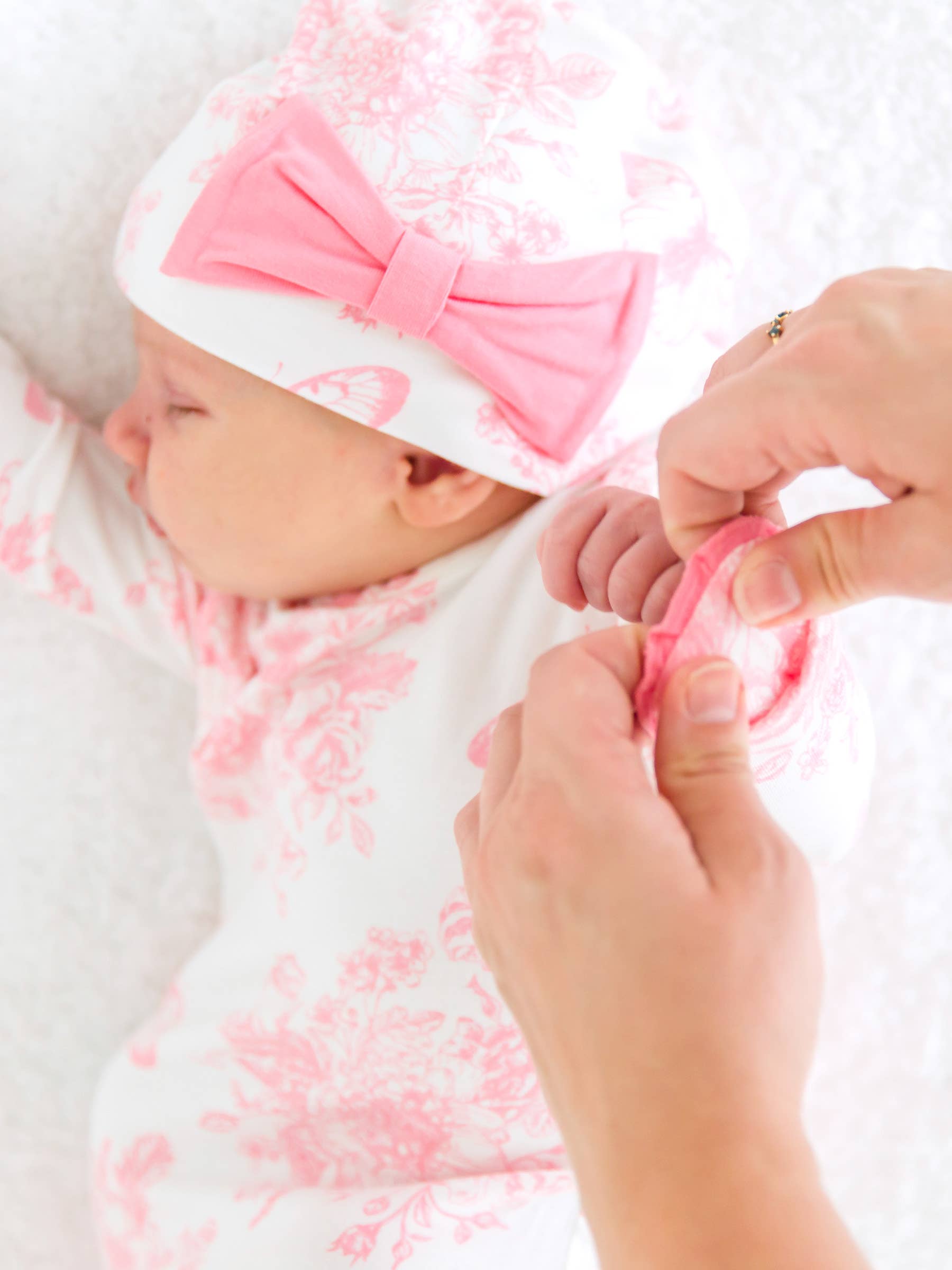 Baby in pink and white toile outfit with a large bow, being held by a person.
